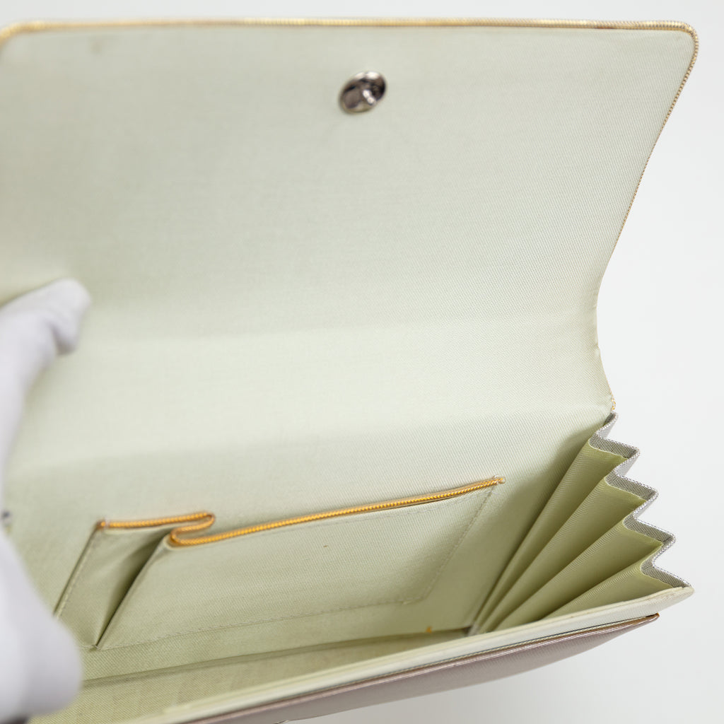 Cream silk lining of a vintage Japanese silk clutch bag held open by gloved hand showing interior pocket trimmed in gold.