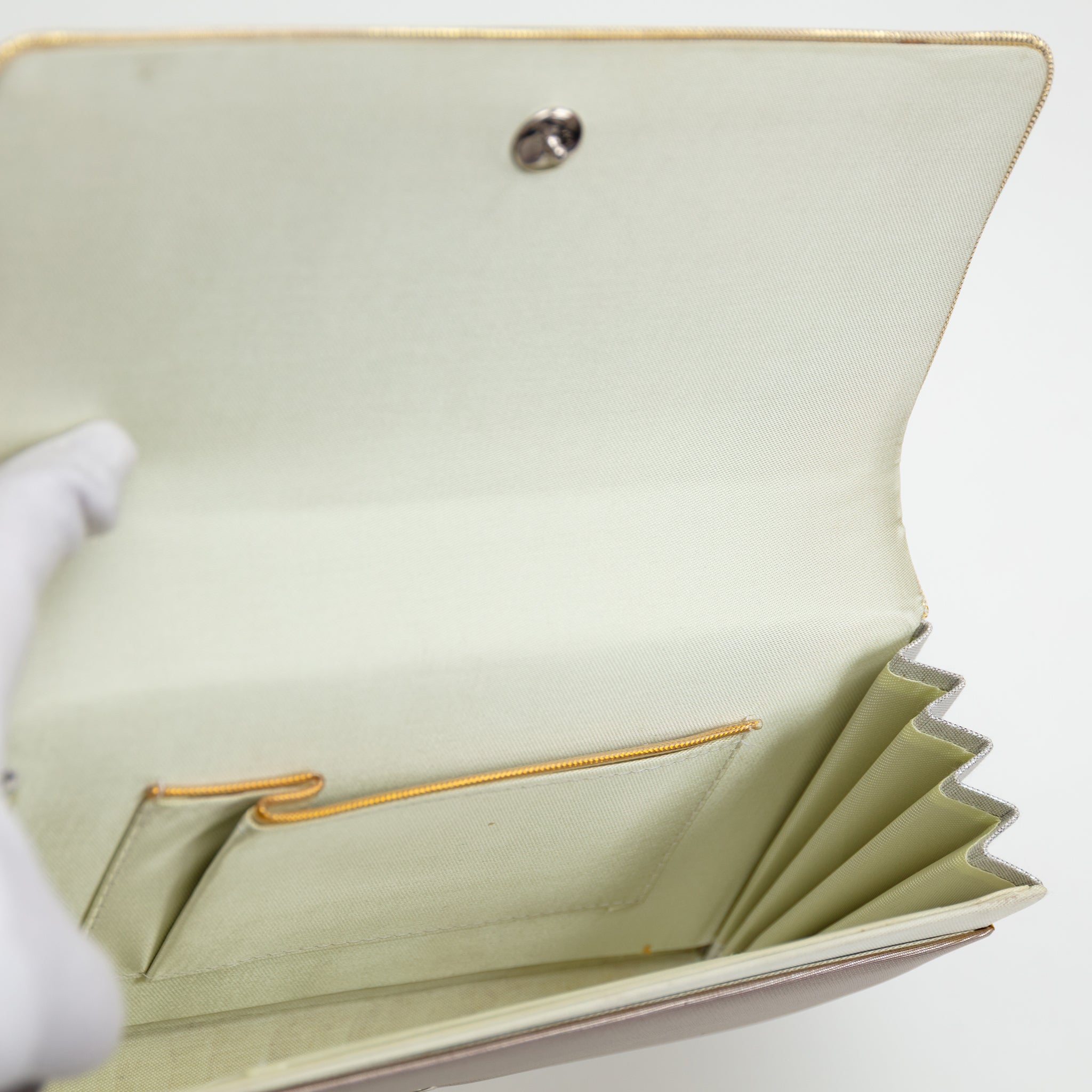 Cream silk lining of a vintage Japanese silk clutch bag held open by gloved hand showing interior pocket trimmed in gold.