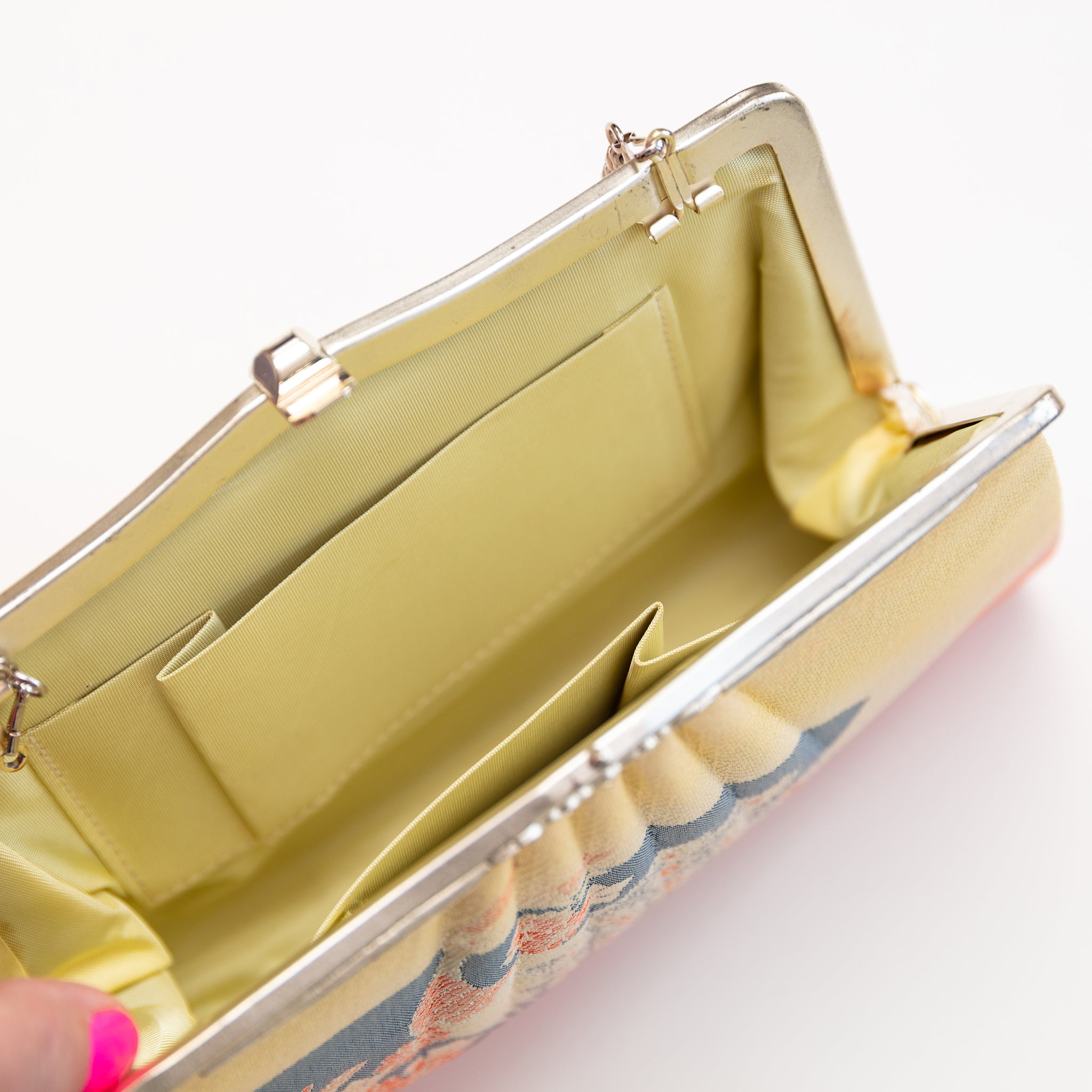Vintage Japanese silk clutch bag held open by a hand showing the yellow silk lining and internal pockets.