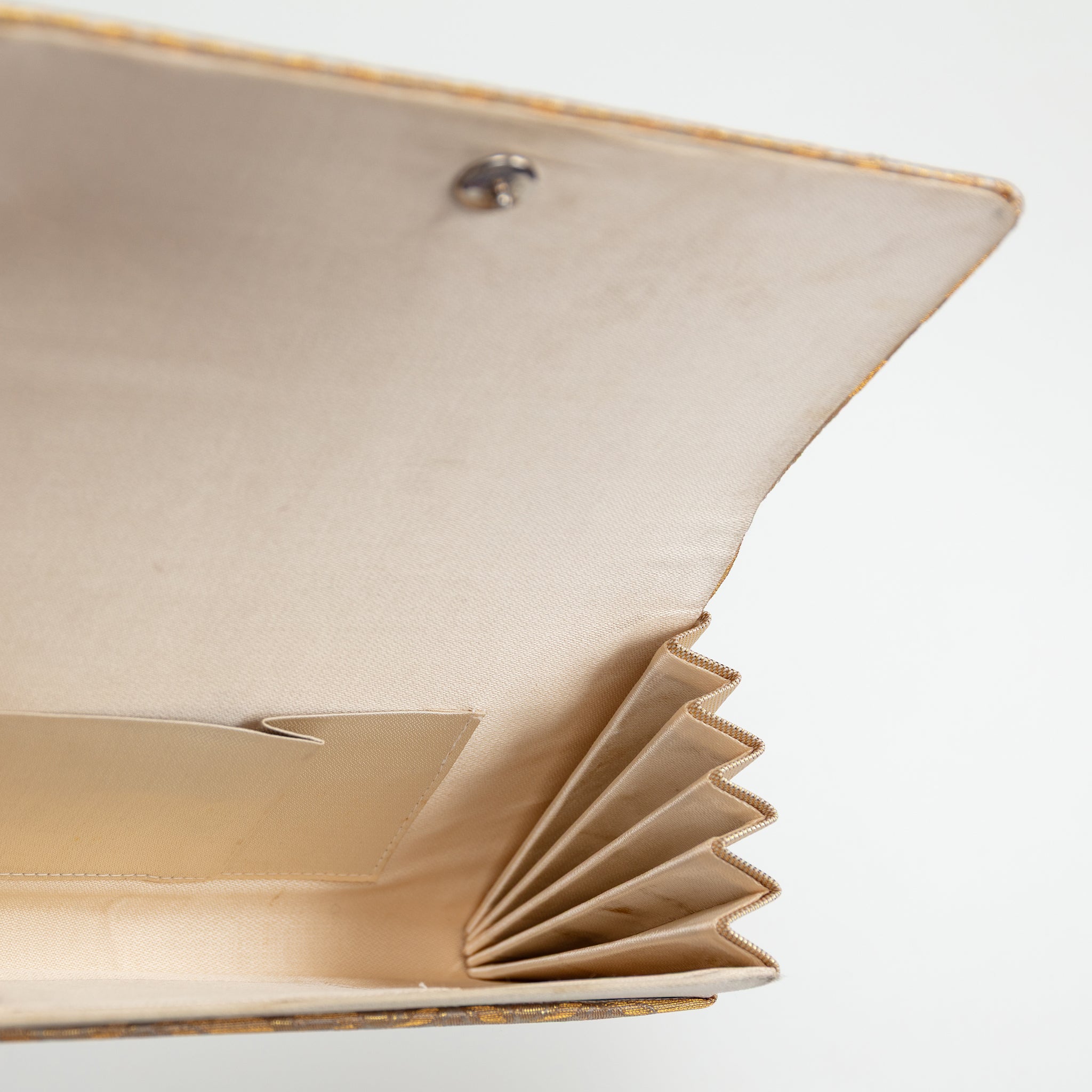 Interior view of a vintage Japanese clutch bag showing the beige silk lining, interior pocket, folded concertina edge and metal fastener.