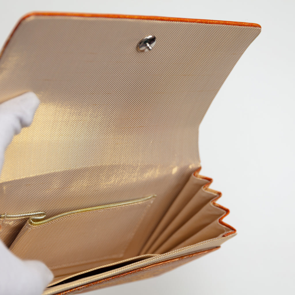 Interior view of a vintage Japanese silk clutch bag being held open by a gloved hand showing the metallic gold silk lining and the interior pockets.