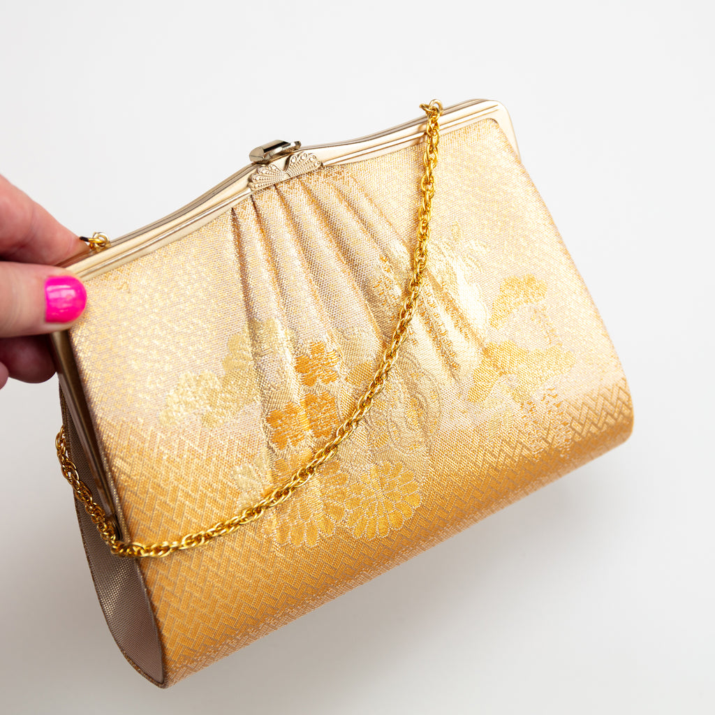 Close up view of vintage Japanese silk clutch bag with gold flowers, basket weave pattern and gold chain, held in a hand.