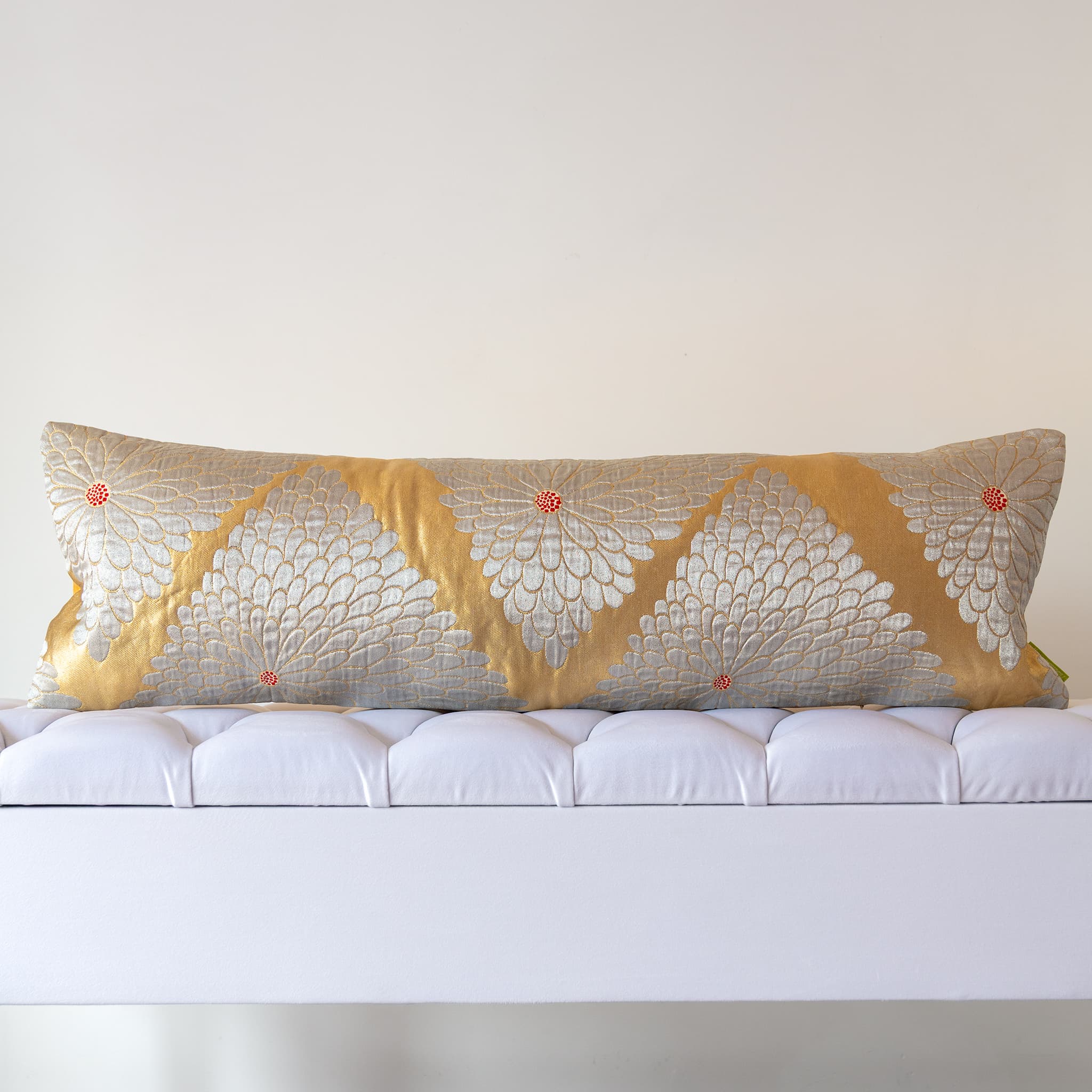 Long gold silk bolster cushion with silver chrysanthemum motifs on white upholstered bench
