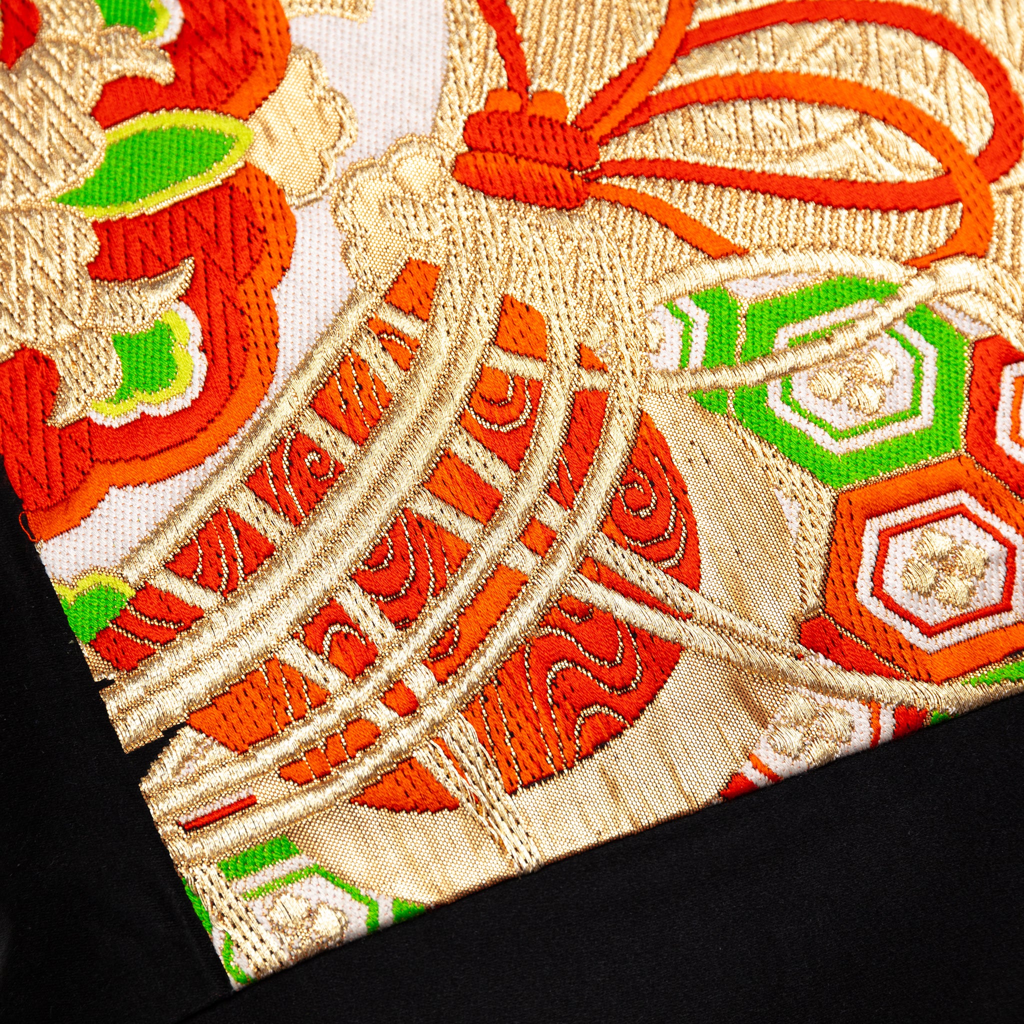 Close-up of the black silk fabric displaying intricate floral drum embroidery and subtle sheen detail on the pillow's corner.