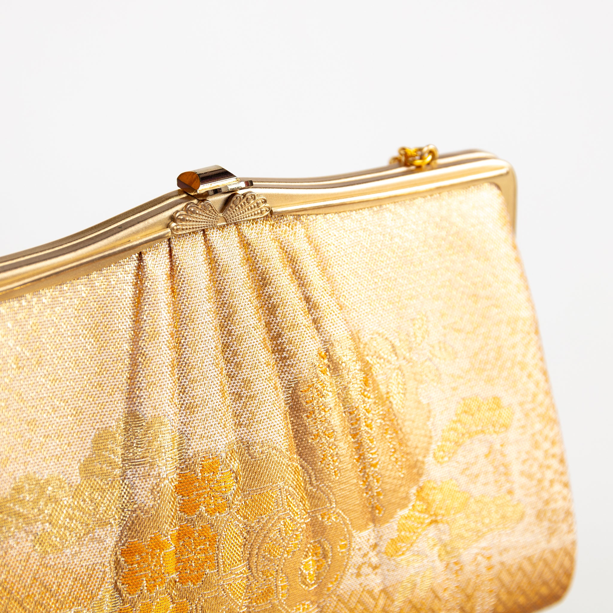 Detail of vintage Japanese silk clutch bag in gold showing decorative metal clasp closure and frame.