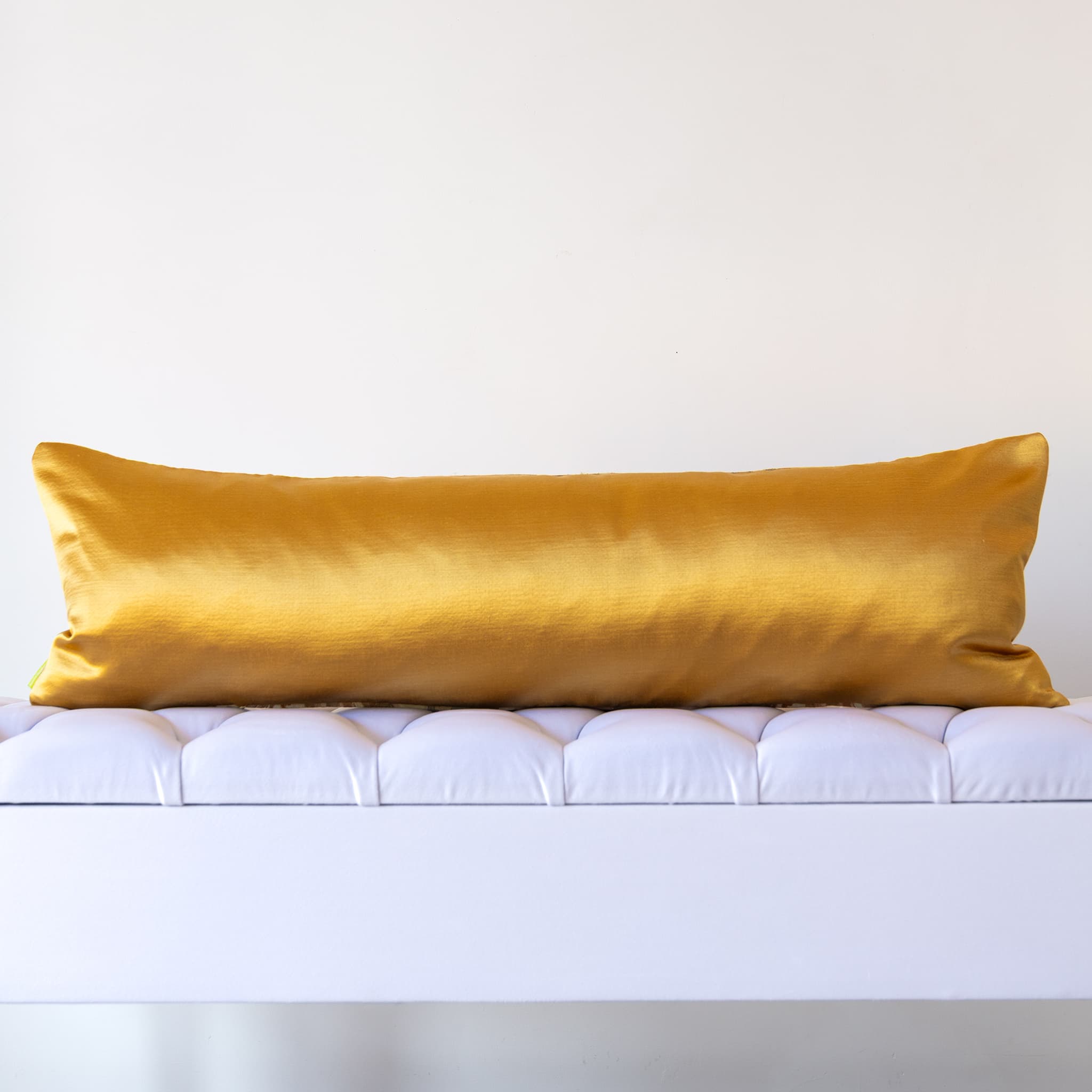 Reverse of gold silk bolster cushion in hammered gold designer satin with luminous glow on a white bench.