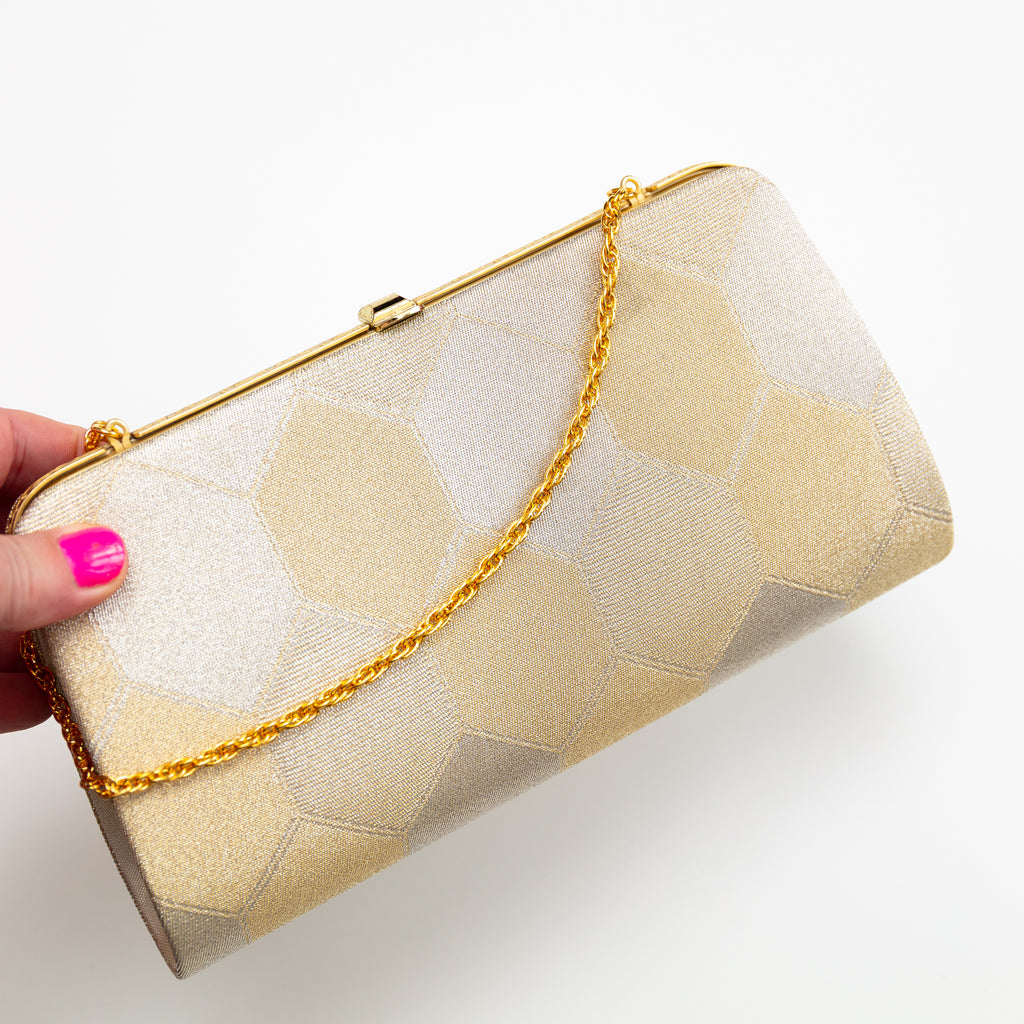Vintage Japanese silk clutch bag in gold with hexagon design, held by a hand, showing gold chain strap and clasp on frame