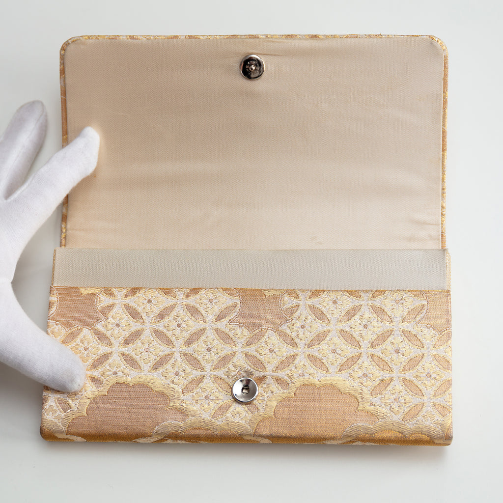 Gold silk vintage Japanese silk clutch bag held open by gloved hand to show silk lining and metal fastener.