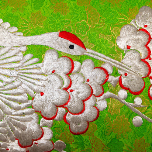 Detail of crane head and plum blossom in silver heavy embroidery over green and gold silk base. Long vintage kimono silk bolster cushion.