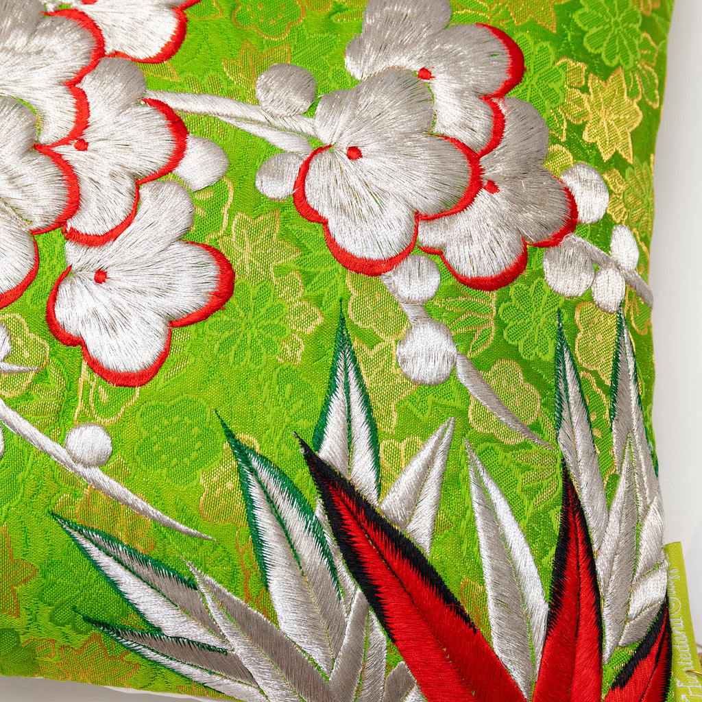 Close up of vintage kimono silk showing embroidered plum blossom and bamboo leaves over green and gold brocade