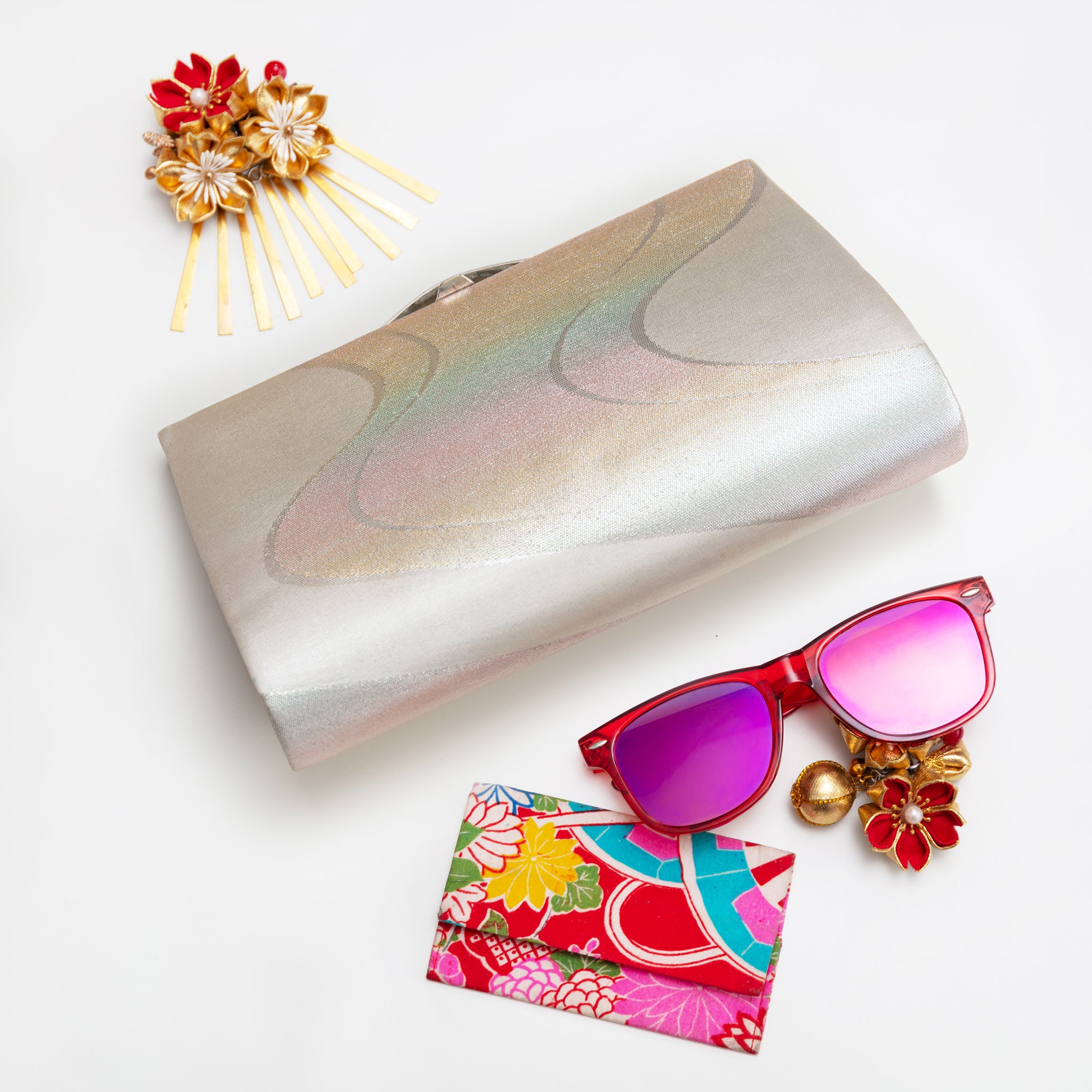 Vintage Japanese silk clutch bag in silver and iridescent colour with sunglasses and decorative items on a white background