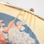 Close up of the vintage Japanese silk clutch bag design of woven peacock, flowers and fans in yellow, peach and black silk and decorative silver metal clasp.