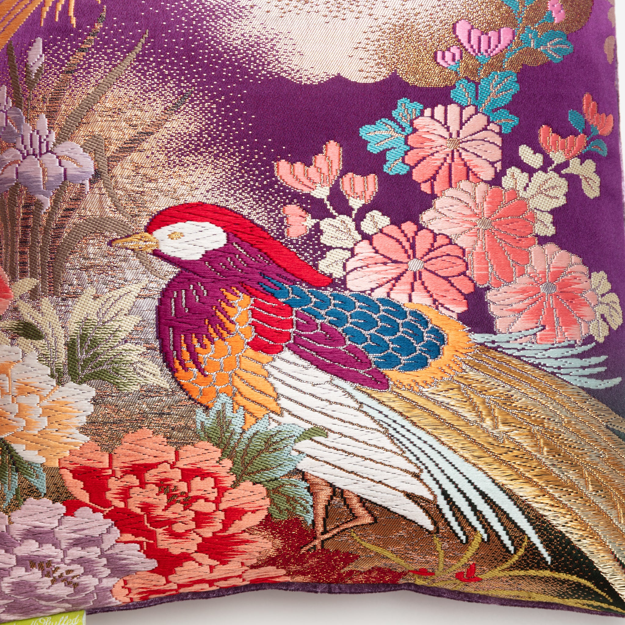 Close-up of the vibrant red silk fabric with intricate flying cranes embroidery atop plush purple velvet bolster edge detail.