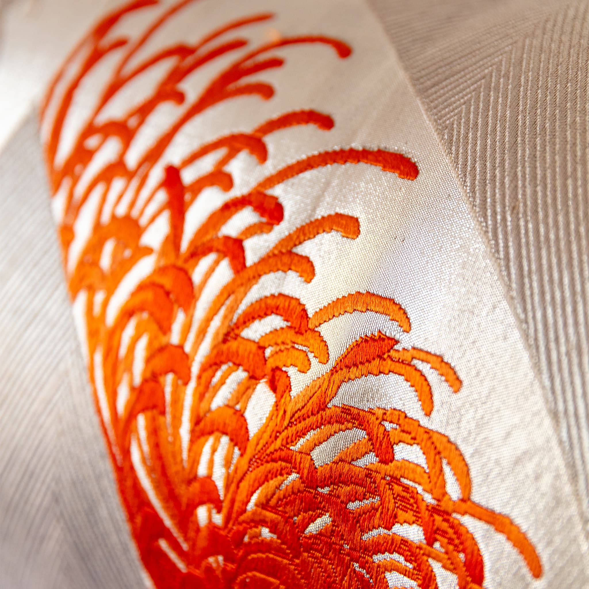 Close up of silver silk bolster cushion showing tight zigzag woven ground with flame orange chrysanthemum motif