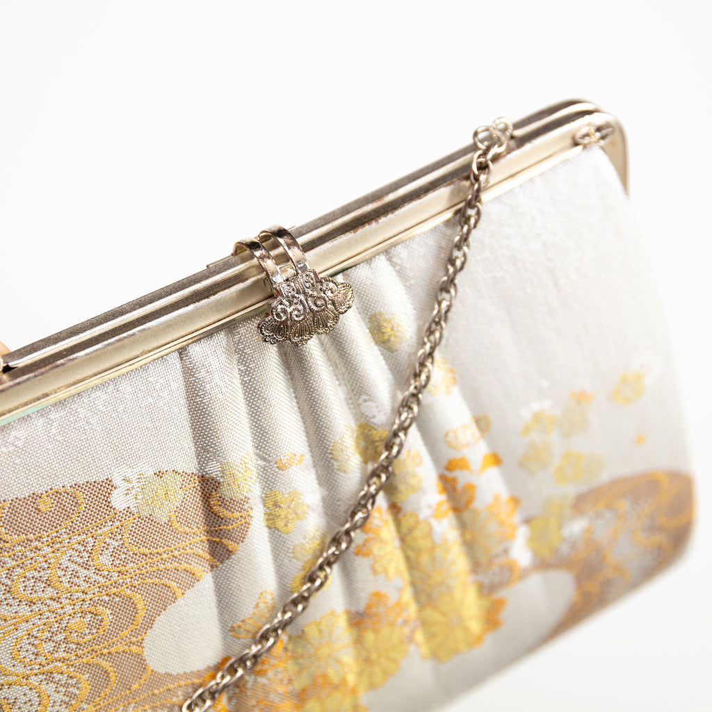 Close up of vintage Japanese silk clutch bag in ivory and gold, silver chain strap and filigree clasp