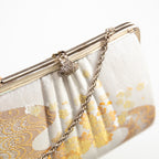 Close up of vintage Japanese silk clutch bag in ivory and gold, silver chain strap and filigree clasp