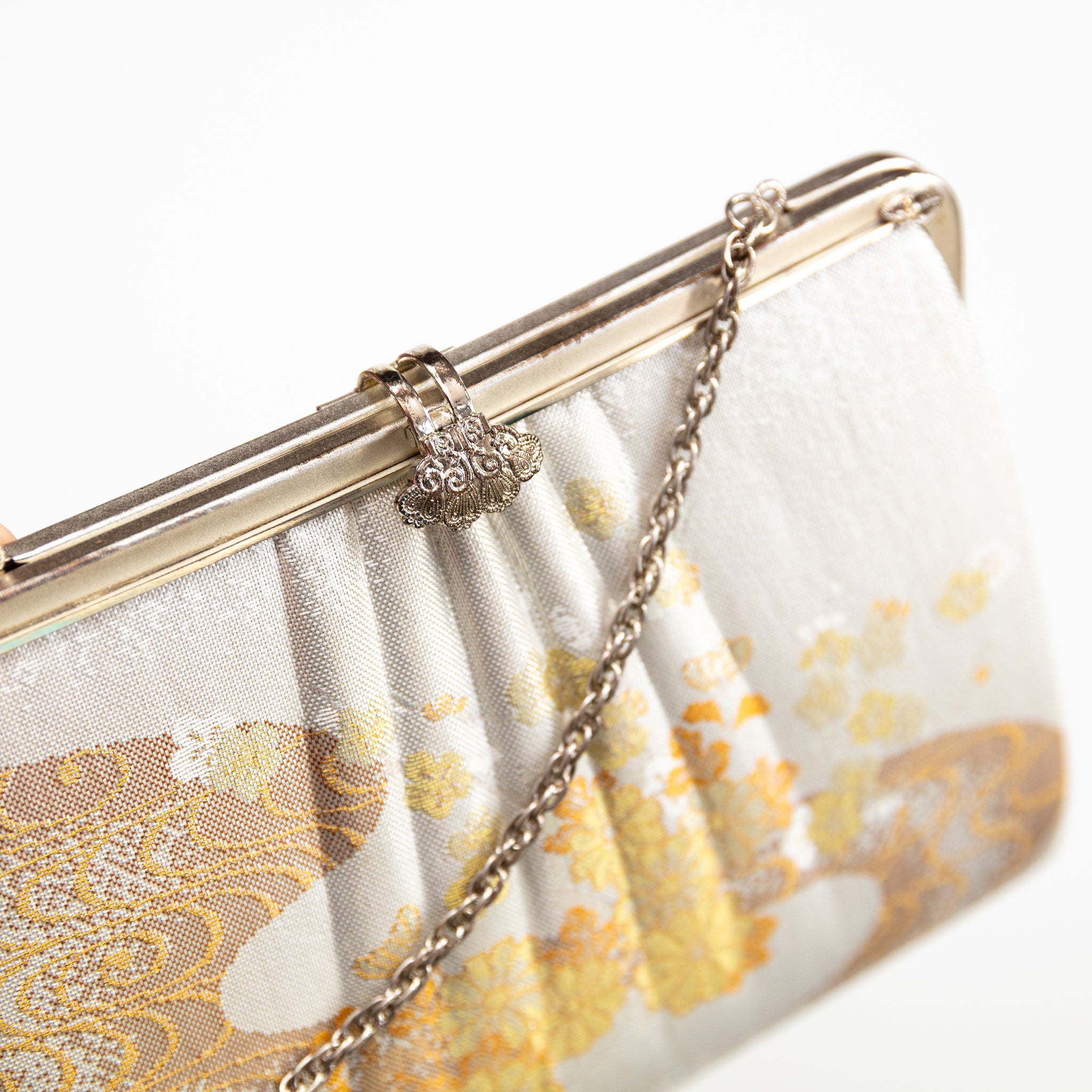 Close up of vintage Japanese silk clutch bag in ivory and gold, silver chain strap and filigree clasp