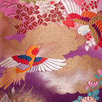 Close-up of the embroidered flying cranes motif on the purple velvet bolster cushion’s textured fabric edge detail.