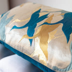 Edge detail of long gold silk bolster cushion showing teal crane motif on vintage obi silk