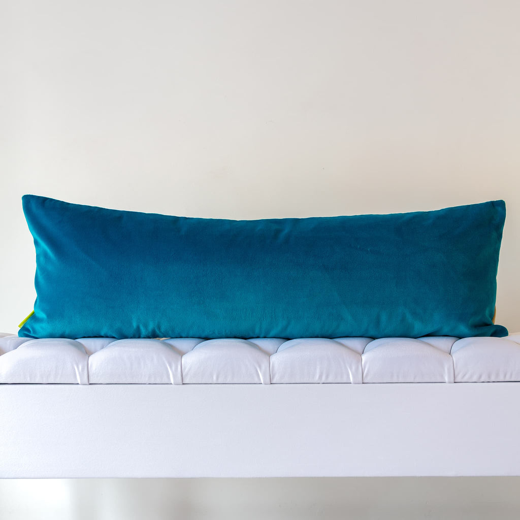 Teal turquoise velvet reverse of long gold silk bolster cushion on a neutral background.