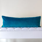 Teal turquoise velvet reverse of long gold silk bolster cushion on a neutral background.