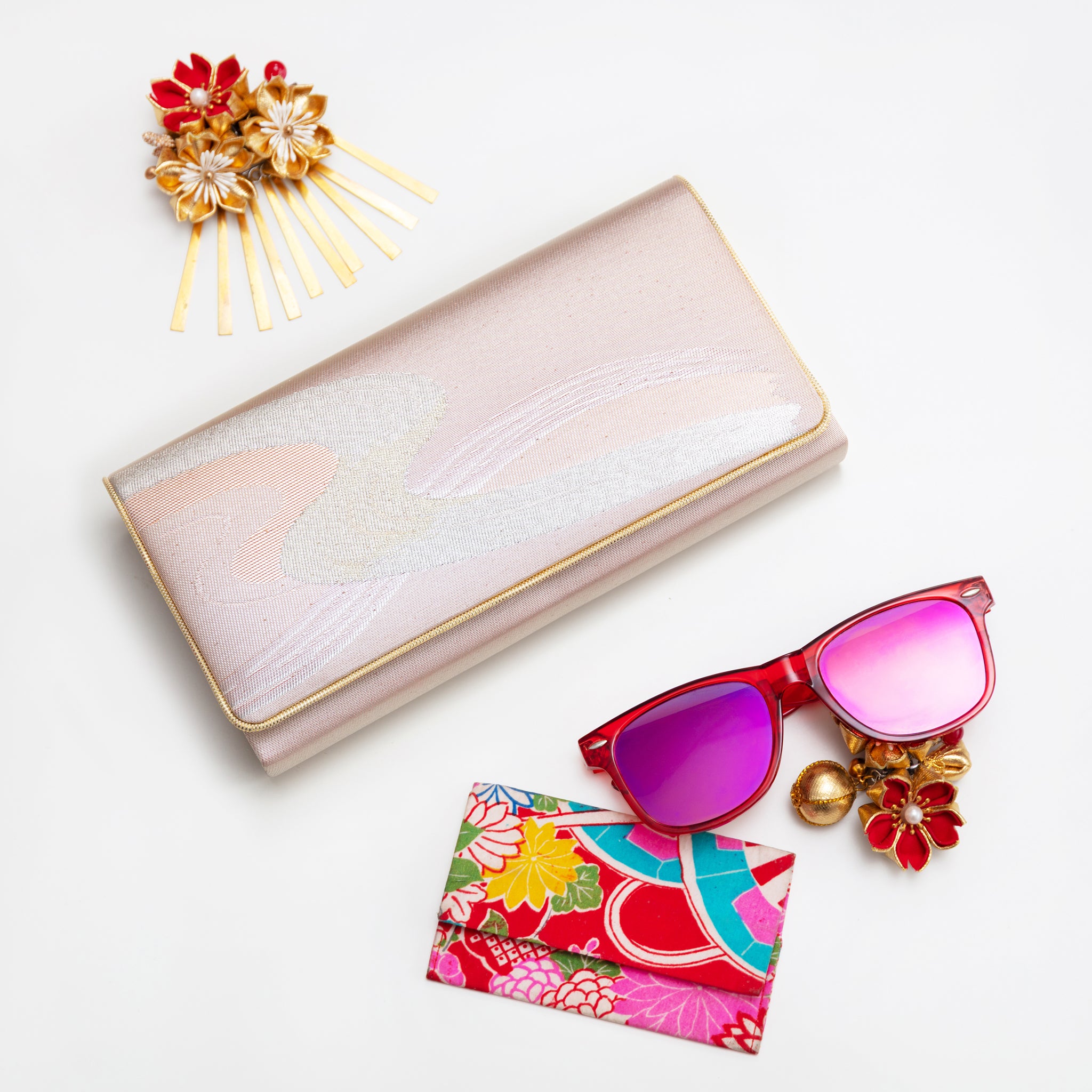 Pink and silver vintage Japanese silk clutch bag with gold trim on white surrounded by accessories.