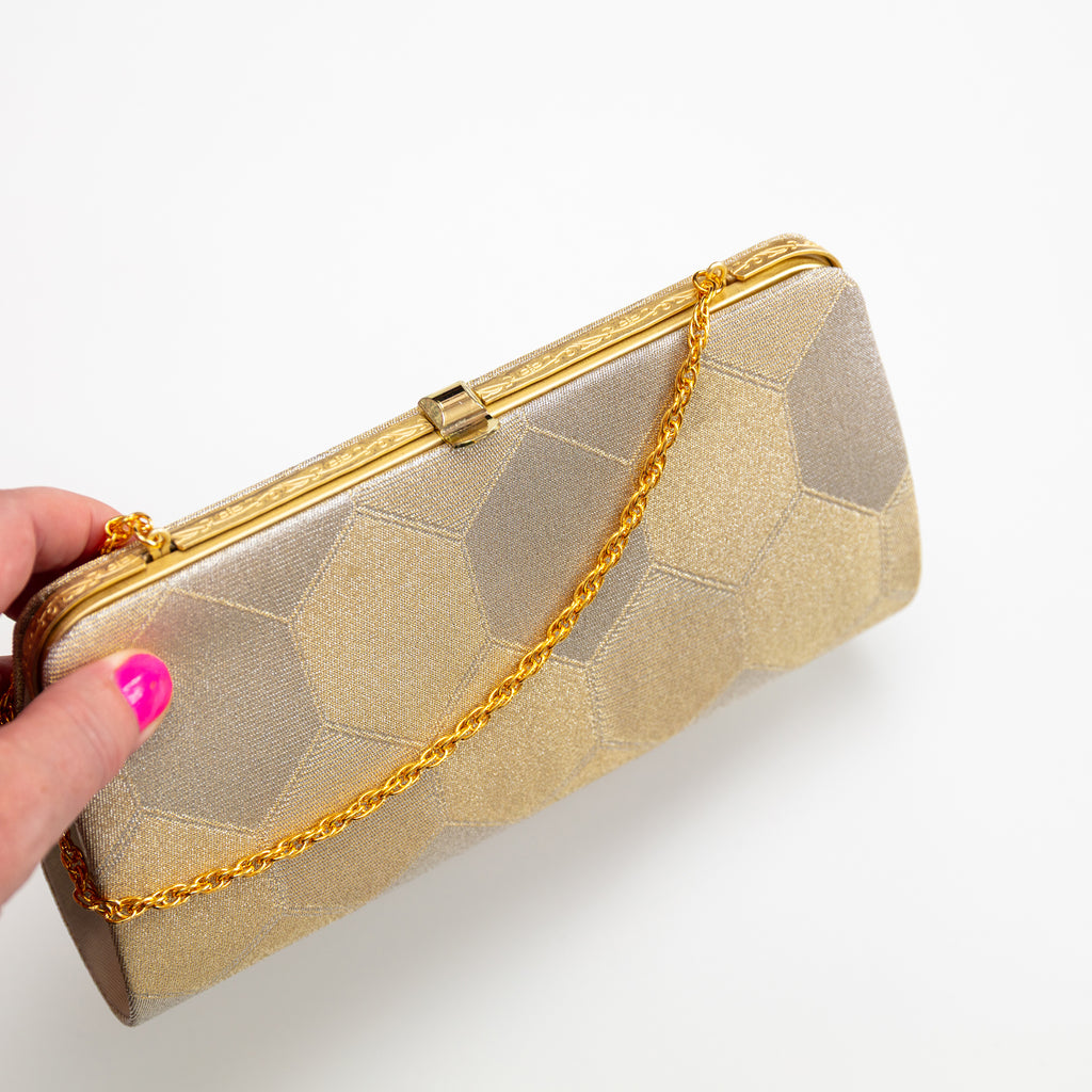 View of top of vintage Japanese silk clutch bag frame showing the bag closed, the decoration on the metal frame and the gold chain strap, help by a hand on white background