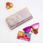 Vintage Japanese fold over clutch bag in lilac with wave pattern on white background and surrounded by accessories.