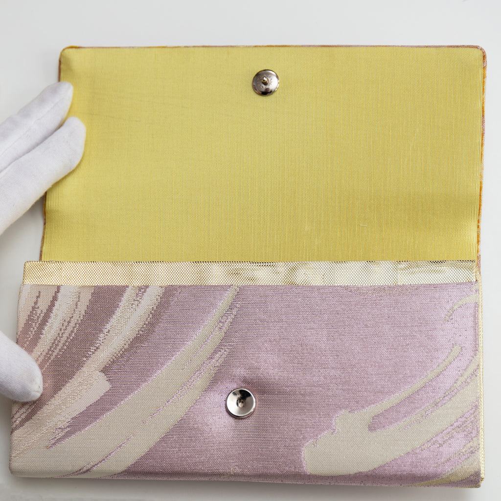 View of vintage Japanese silk clutch bag held open by a gloved hand showing gold and cream silk lining and metal fastener.
