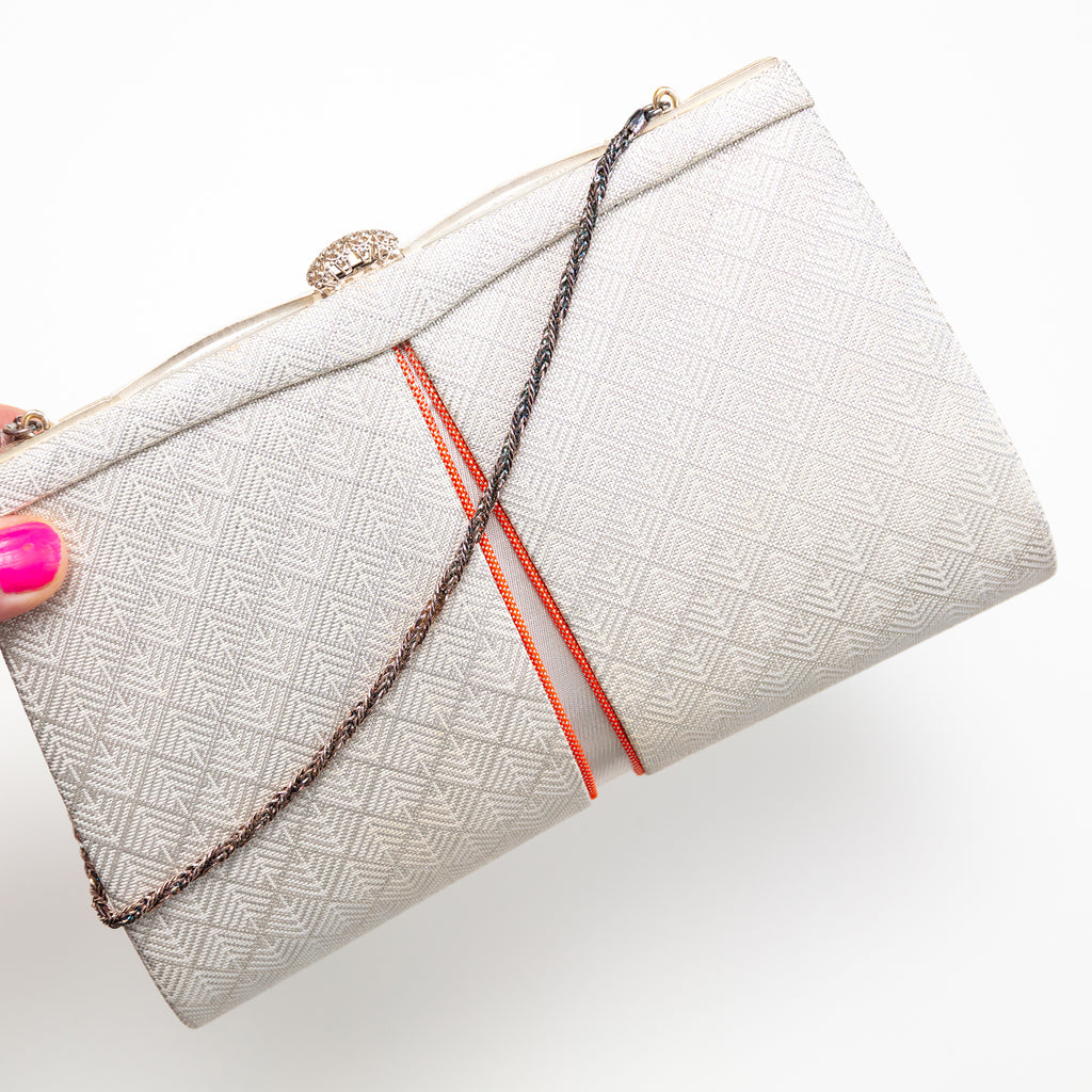 White geometric pattern vintage Japanese silk clutch bag with orange accents held by a hand on a white background