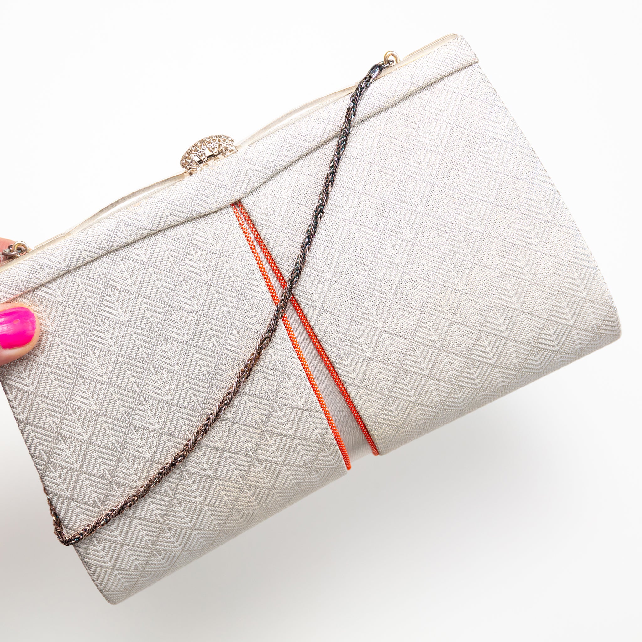 White geometric pattern vintage Japanese silk clutch bag with orange accents held by a hand on a white background