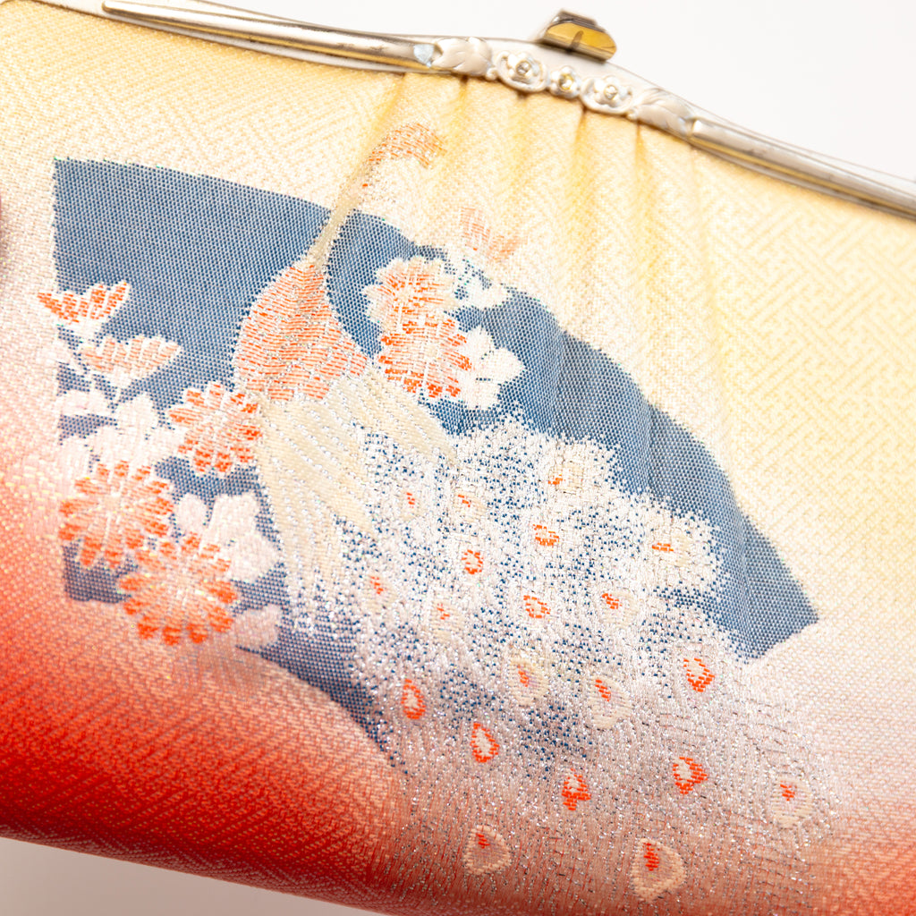 View of the main design on the front of the vintage Japanese silk clutch bag showing patterned silk in geometric pattern, black fan shape and peacock in gold.