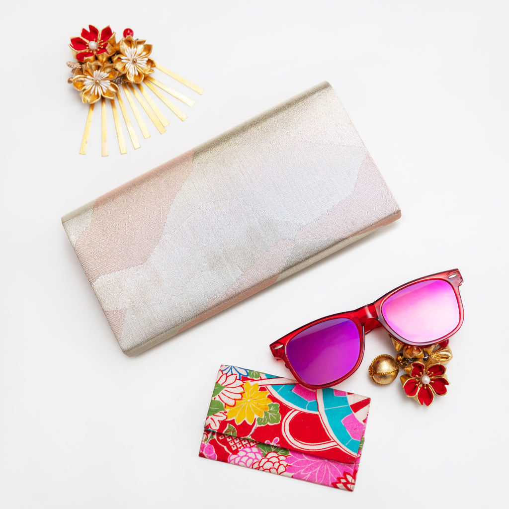 Silver metallic vintage Japanese silk clutch bag on white with accessories and sunglasses.