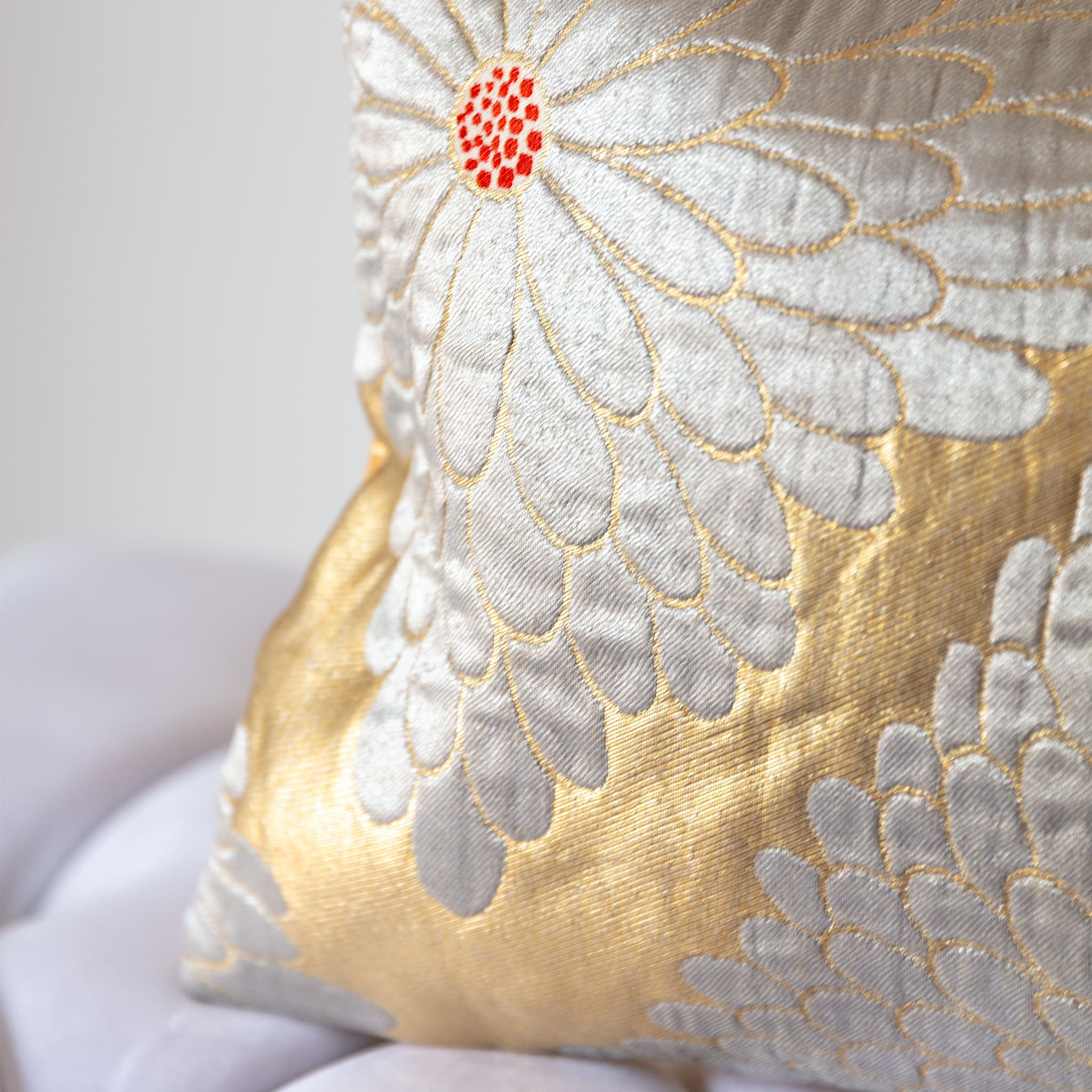 Corner detail of gold silk vintage kimono bolster cushion with silver flower and red centre.