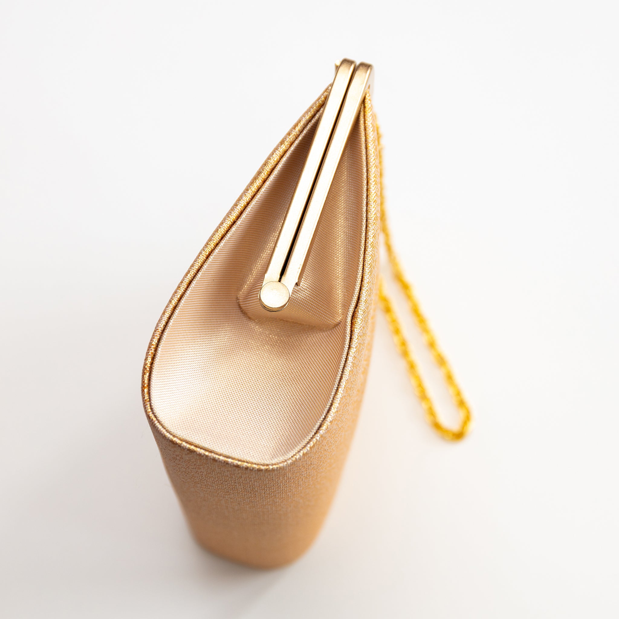 Vintage Japanese gold evening bag showing side view of the gold metal frame and gold silk side panel, on white