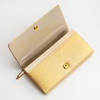 Vintage metallic gold clutch bag with flap open to show the beige silk lining and gold metal stud fastening.