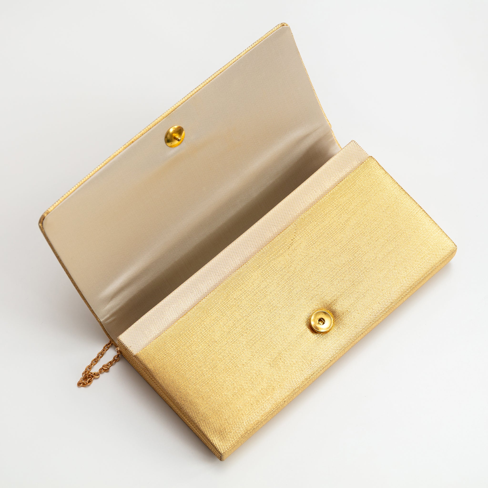 Vintage metallic gold clutch bag with flap open to show the beige silk lining and gold metal stud fastening.