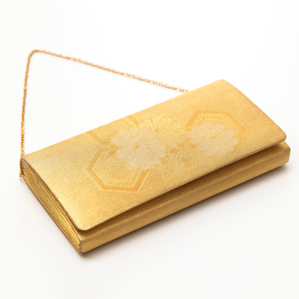 View of a vintage Japanese silk clutch bag lying on a white surface with the gold metal chain strap visible. Floral pattern on the front.