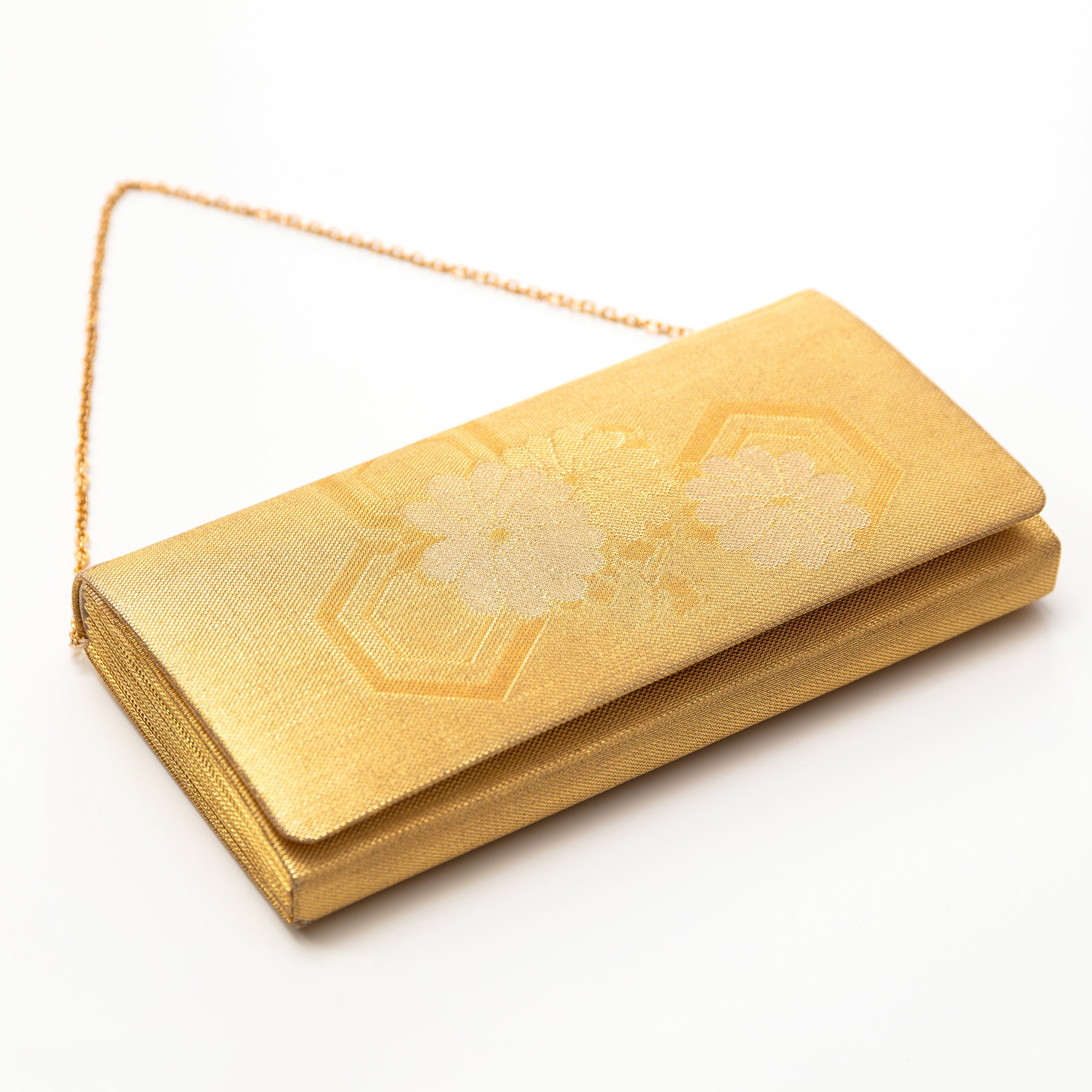 View of a vintage Japanese silk clutch bag lying on a white surface with the gold metal chain strap visible. Floral pattern on the front.