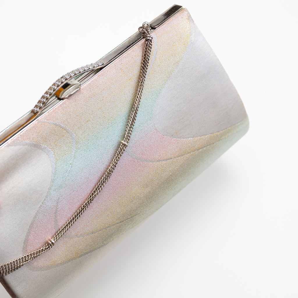 Close up of vintage Japanese clutch bag in iridescent silver silk with river pattern. The bag is closed and the decorative silver chain strap drapes over the front of the bag.