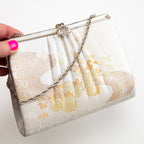 Front view of vintage Japanese silk clutch bag held in hand, silver chain handle and decorative silver metal clasp. 
