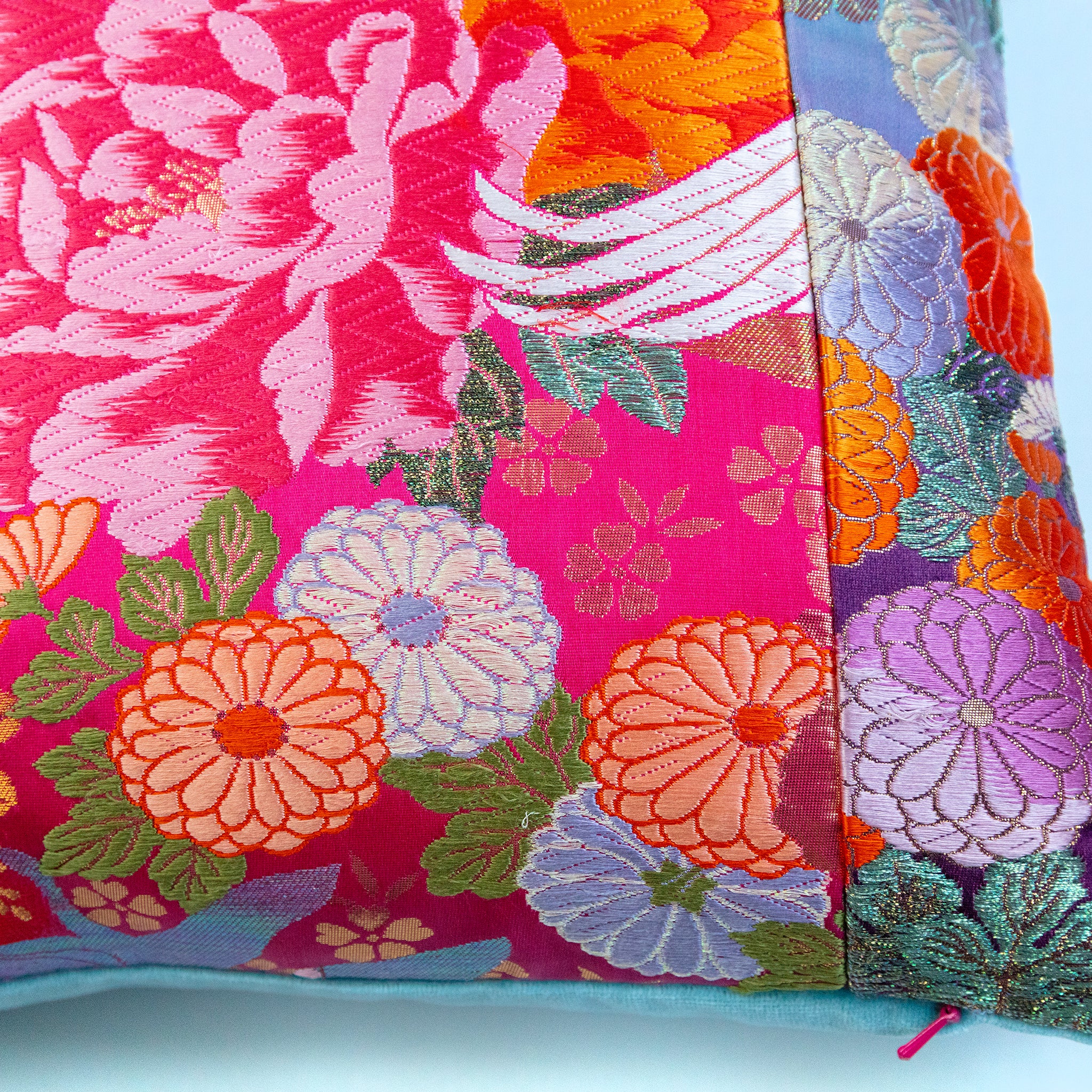Close-up of the vibrant blue and pink embroidered crane details on the cushion's textured teal velvet surface, highlighting