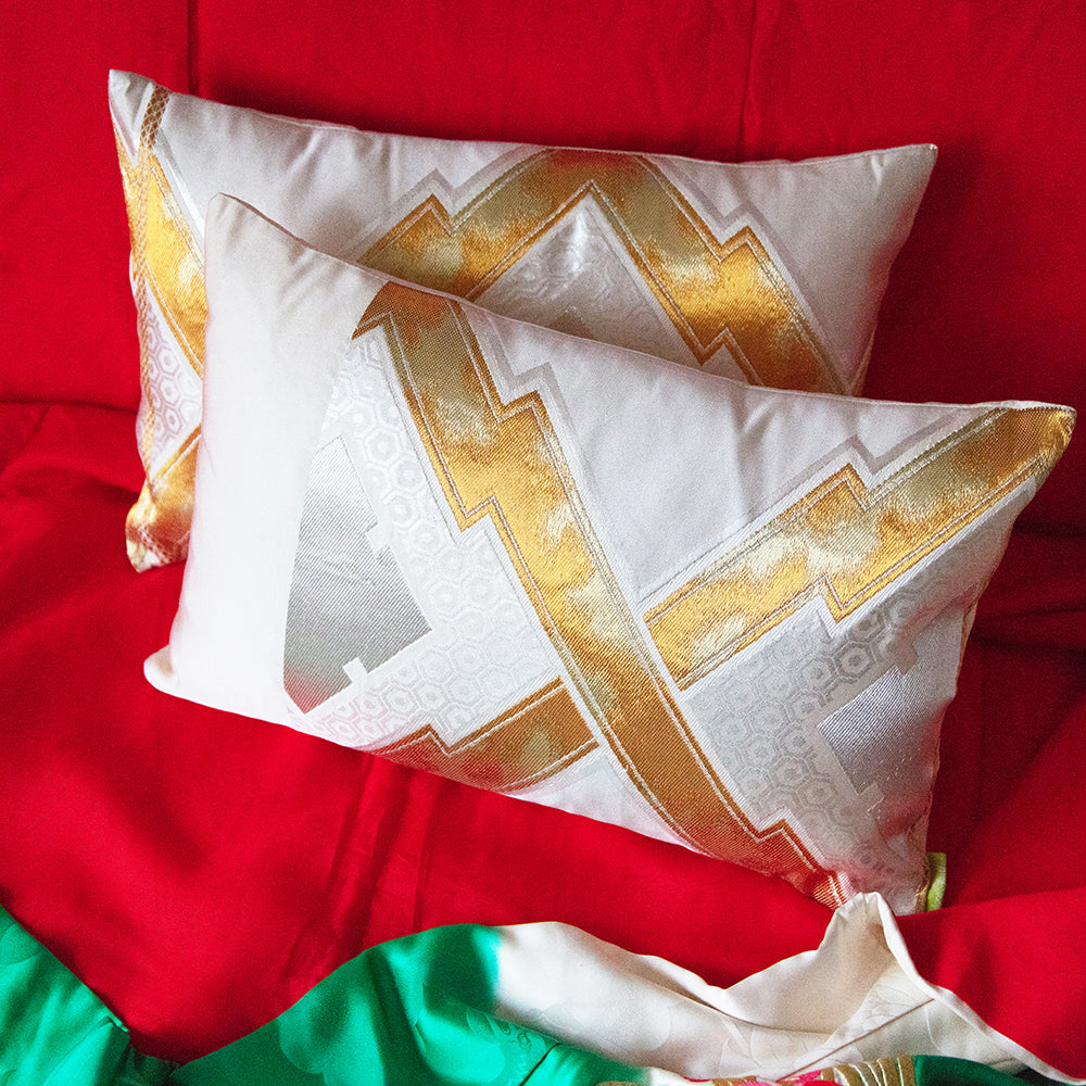 Two cream, gold and silver vintage obi pillows on a bright red silk throw on a sofa.