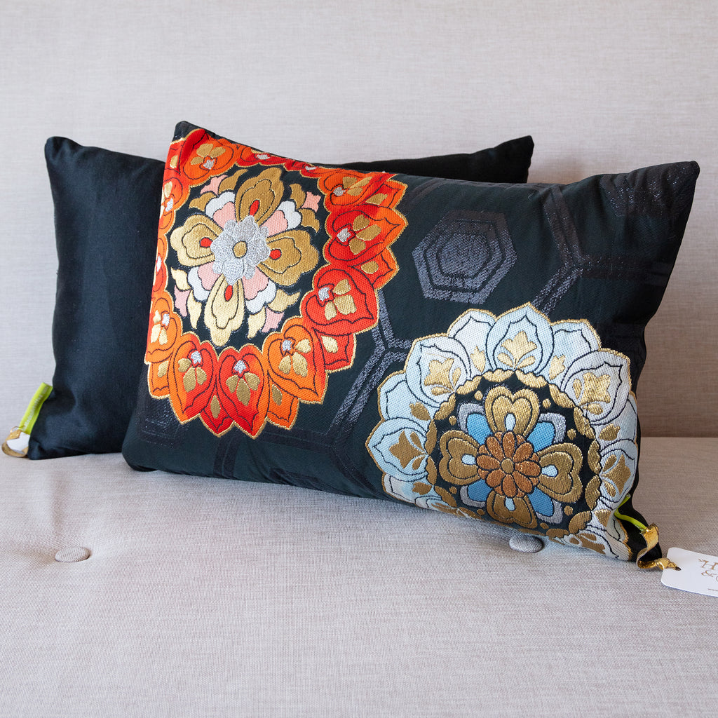 Rectangular black silk vintage obi cushion with red and blue flowers with gold accents, plain black cushion behind, on neutral sofa.