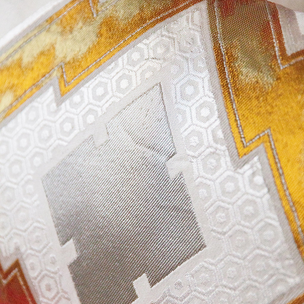 Pine bark diamond pattern in gold and silver over cream hexagon pattern. Close up detail of a vintage Japanese obi cushion.