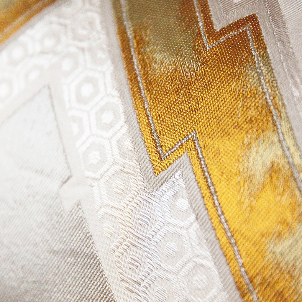 Close up of the gold woven highlight on a vintage kimono cushion, the gold has different tones in the weave. Over a cream hexagon woven pattern.
