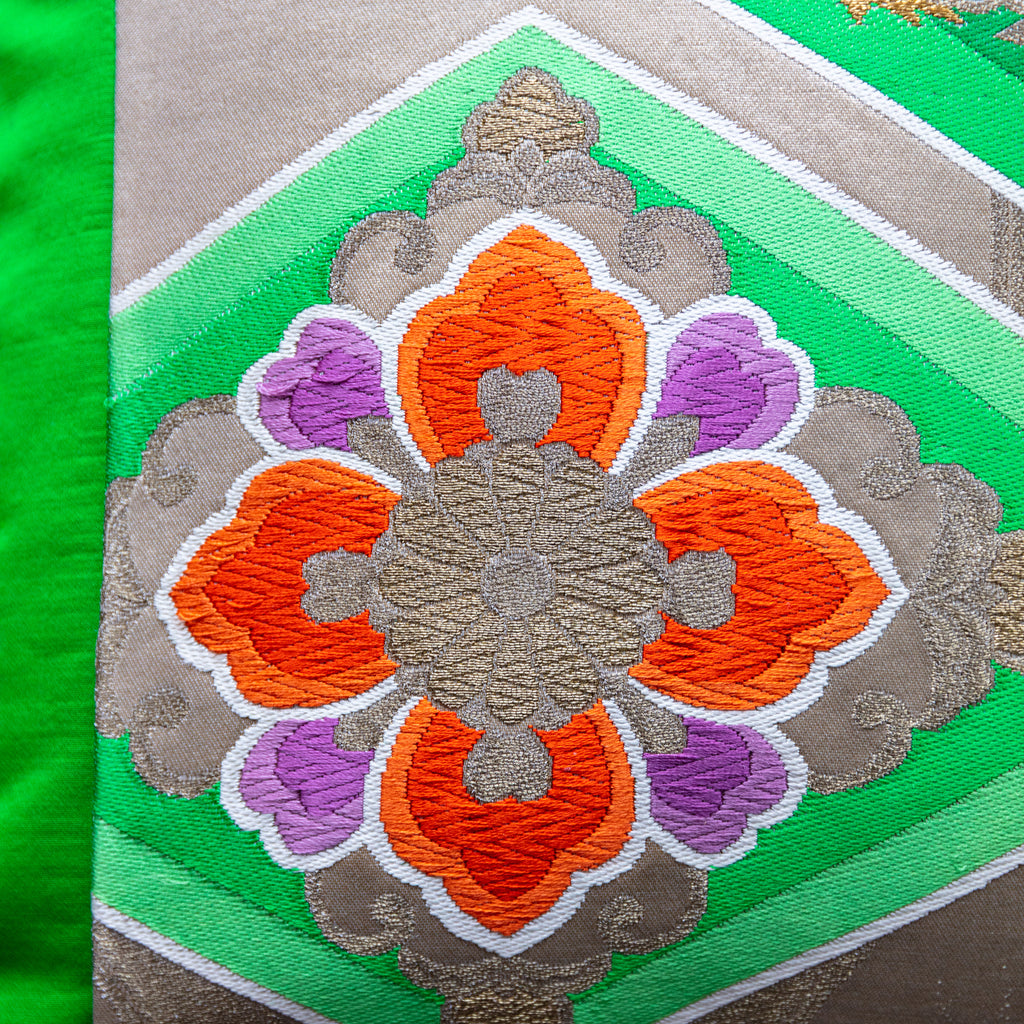 Close-up of green obi silk fabric displaying intricate gold floral embroidery and rich velvet backing at a diagonal angle