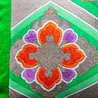 Close-up of green obi silk fabric displaying intricate gold floral embroidery and rich velvet backing at a diagonal angle