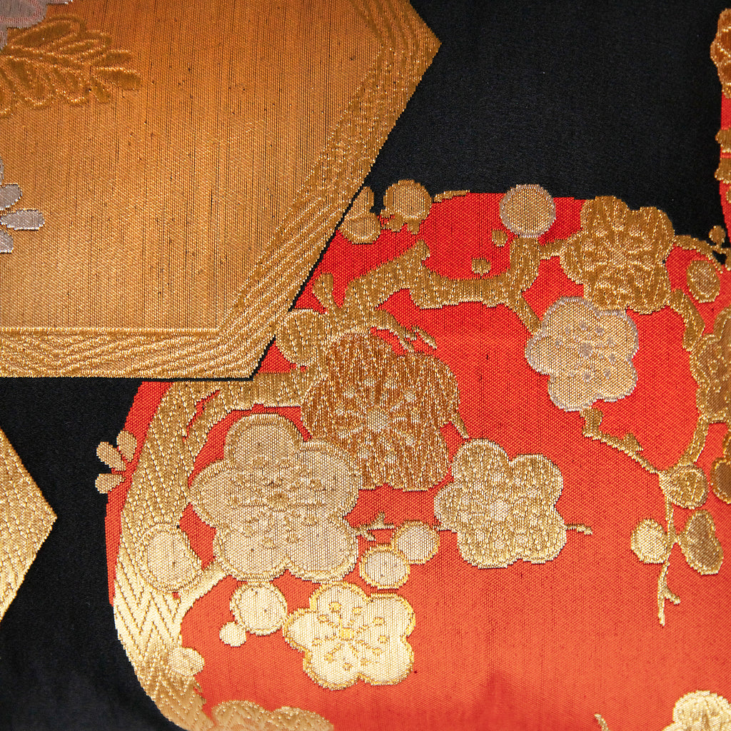 Close-up of black obi silk pillow  showing intricate gold and orange floral motifs with textured embroidered details.