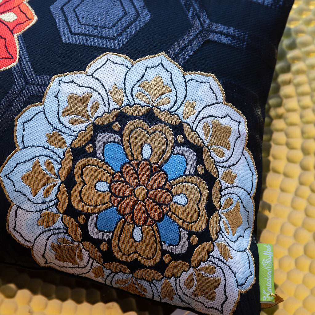 Detail of black silk pillow with hexagon pattern and a large blue and gold floral motif in the corner.